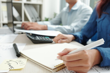 Businesswoman sitting next to colleague and filling planner with plans and creative ideas