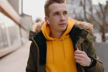 Handsome stylish man walks in a winter city with wireless earbuds in his ears