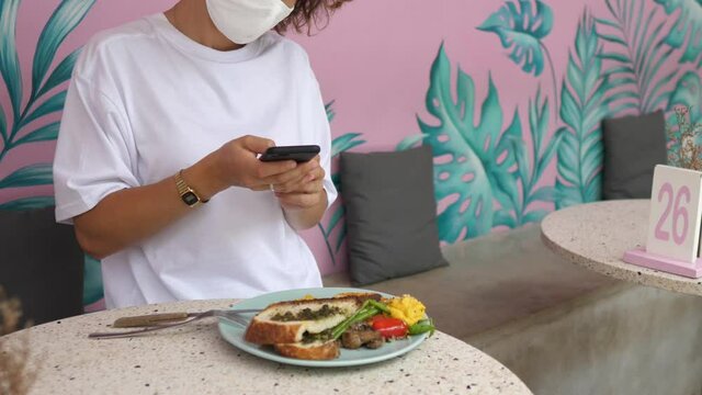 A girl in a protective face mask taking pictures of her lunch. Sharing your food on social media concept