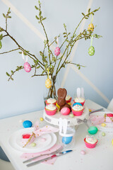 spring holidays concept - close up of decorated table with cupcakes, colorful painted eggs and chocolate bunny