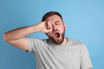 Sleepy young man yawning on light blue background