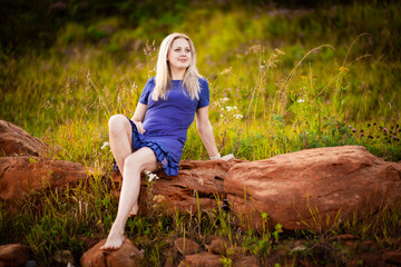 Beautiful young blonde in blue dress sitting on red rocks, Selective focus
