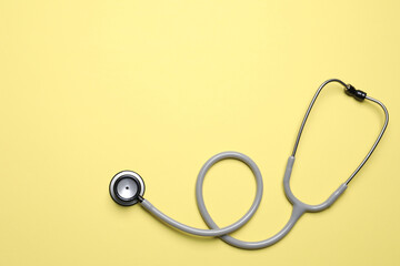 Stethoscope on yellow background, top view. Space for text