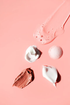 Various cosmetic smears on a pink background, top view. Lather soap foam, aloe vera clear transparent spot, facial moisturizer, body milk lotion and lipstick texture