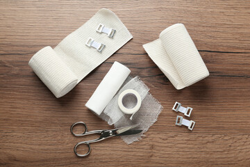 Medical bandage rolls, sticking plaster and scissors on wooden background, flat lay