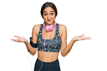 Beautiful brunette woman wearing gym clothes and using headphones clueless and confused expression...