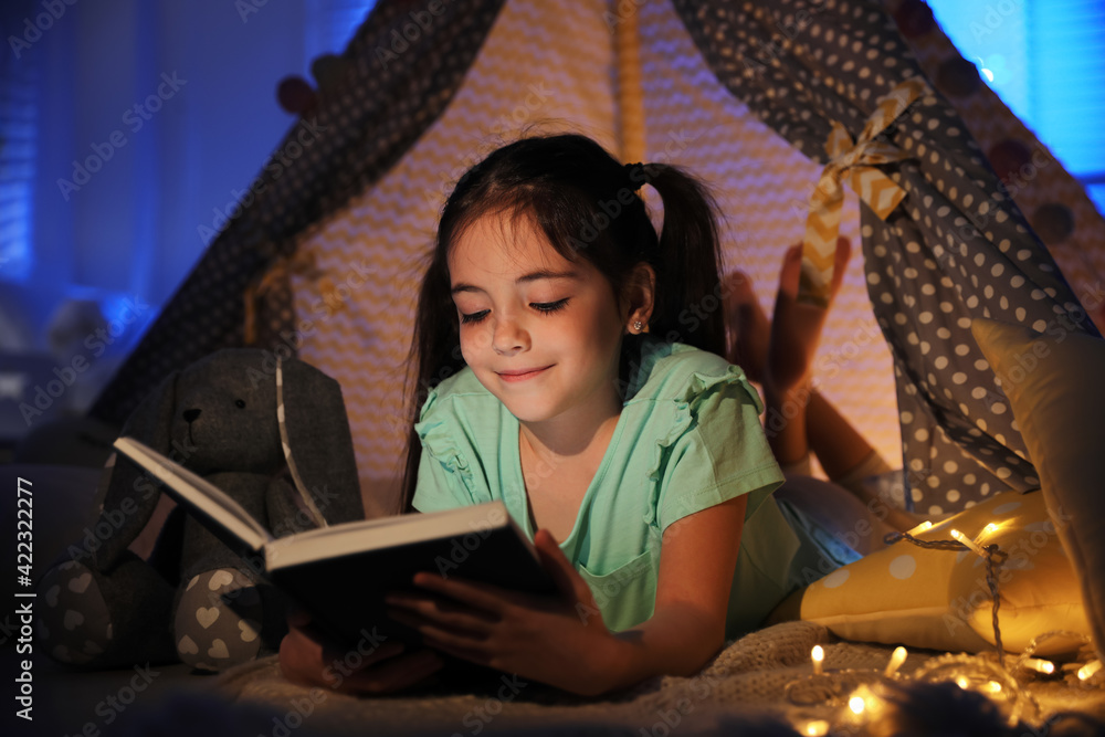 Wall mural Little girl reading fairy tale in play tent at home