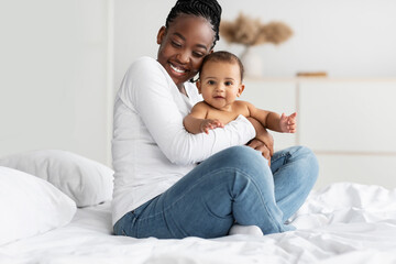 Fototapeta premium Black mom sitting on bed with her cute baby