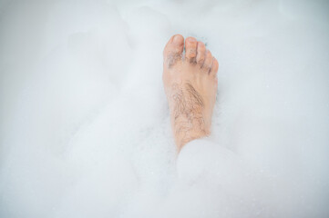 Fototapeta premium Funny picture of a man taking a relaxing bath. Close-up of male feet in a bubble bath