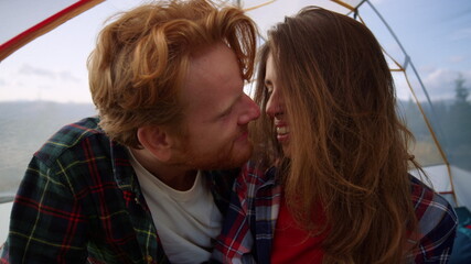 Romantic couple cuddling together in tent. Smiling woman and man touching noses