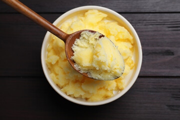 Bowl and spoon of Ghee butter on wooden table, top view