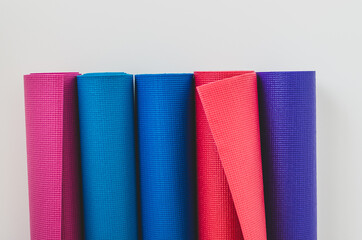 Close up of colourful rolled yoga mats in a yoga studio by a white wall background