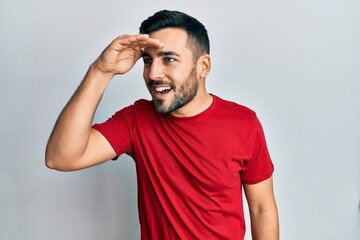 Young hispanic man wearing casual clothes very happy and smiling looking far away with hand over...