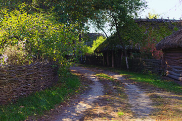 Pereyaslav, Ukraine-October 14,2020:Winding narrow dirt village road. Picturesque landscape of ancient Ukrainian village. Wooden houses with trees and flowers at the front yard behind the wicker fence