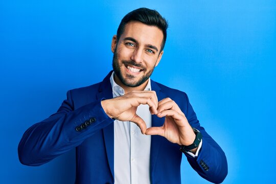 Young hispanic businessman wearing business jacket smiling in love doing heart symbol shape with hands. romantic concept.