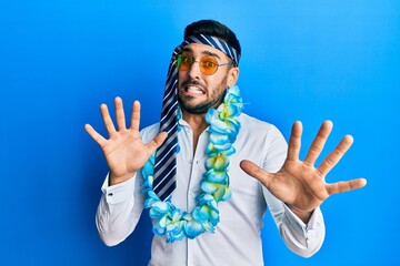 Young hispanic businessman wearing party funny style with tie on head afraid and terrified with fear expression stop gesture with hands, shouting in shock. panic concept.