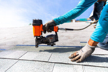 roofer installing roof shingles with nail gun - obrazy, fototapety, plakaty