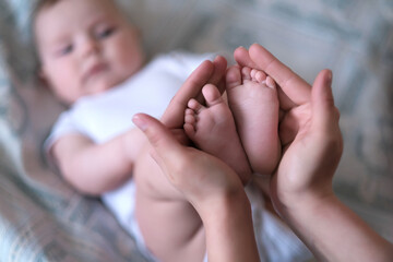 Mom holds the baby's tiny legs in her hands. Selective focus on heels and toes