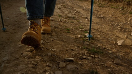 Girl in stylish boots walking on dirt road. Female tourist trekking in mountains