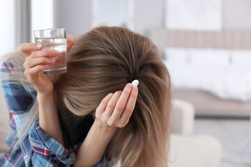 Upset young woman with abortion pill and glass of water at home - obrazy, fototapety, plakaty