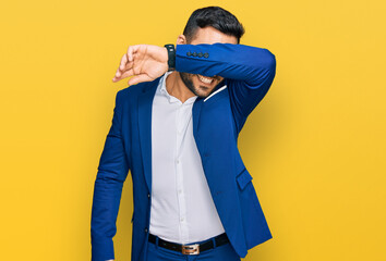 Young hispanic man wearing business jacket covering eyes with arm smiling cheerful and funny. blind concept.