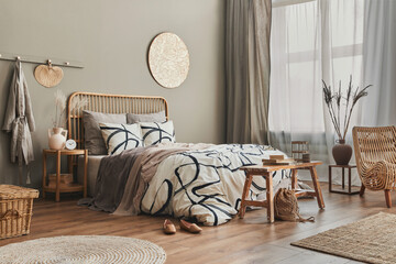 Stylish composition of bedroom interior with wooden bed, furniture, dried flowers in vase, rattan...