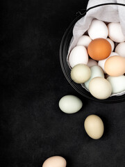 Fresh white chicken eggs in a metal basket with a napkin, top view, on a black textured background. Creativity.