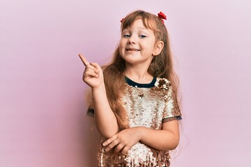 Little caucasian girl kid wearing festive sequins dress with a big smile on face, pointing with hand and finger to the side looking at the camera.