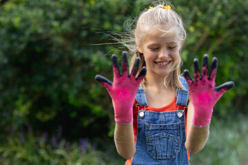 Smiling caucasian girl in garden holding up hands wearing dirty pink gardening gloves