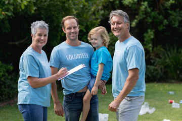 Caucasian senior couple with father and son in volunteer shirts smiling in littered field