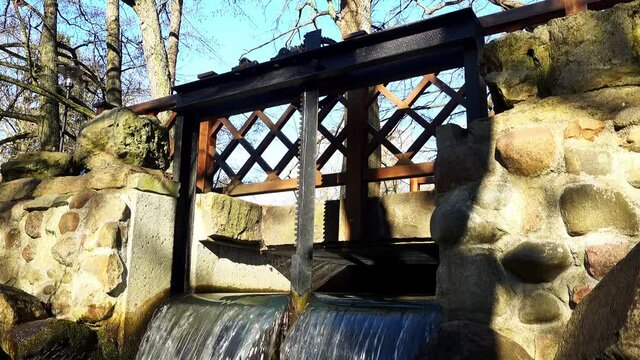 Water Lock Gate Control Gears with Cogwheels On Canal with Waterfall and Rocky Stream underneath on Bright Sunny Morning
