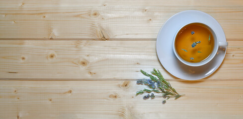 A cup of tea with thyme on a wooden table.