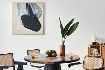 Stylish composition of dining room interior with design table, modern chairs, decoration, tropical leaf in vase, fruits, abstract mock up paintings and elegant accessories in home decor. Template.