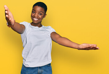 Young african american woman wearing casual white t shirt looking at the camera smiling with open arms for hug. cheerful expression embracing happiness.