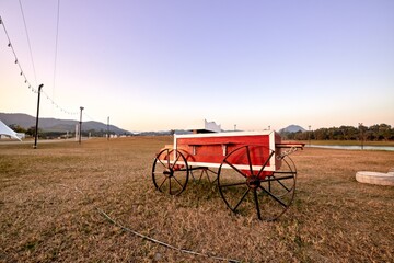 Fototapeta premium Red cart is parking in meadow, at evening