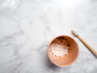 Bamboo toothbrush and dental tabs on a white marble background, plastic free swap.