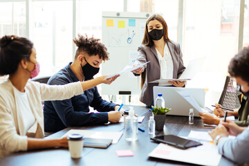 Business team wearing protective masks while meeting in the office during the COVID-19 epidemic. Woamn shares documents with colleagues