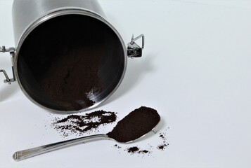 Cuban coffee in a metal container and a spoon full of coffee grounds on a white background with...