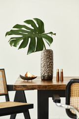 Modern concept of dining room interior with wooden table, chairs, plate with nuts, salt and pepper shaker and tropical leaf in vase. White wall. Template. Detalis.