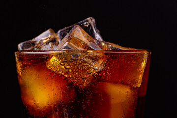 Fizz sparkling cola water refreshing bubbly soda pop with Ice cubes. Glass of cola on black...