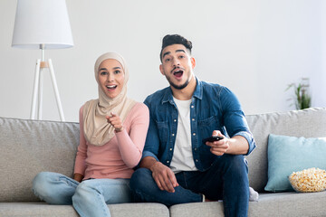Excited middle-eastern couple switching TV channels at home