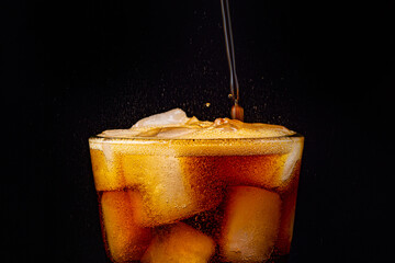 Fizz sparkling cola water refreshing bubbly soda pop with Ice cubes. Glass of cola on black...