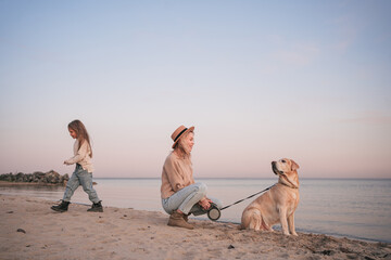 Young mother and daughter walk with dog on the beach