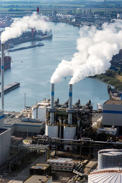 Air pollution from chimney exhaust at a waste processing plant in a large industrial port.