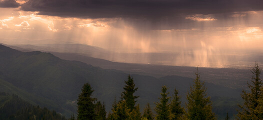 Fototapeta na wymiar The rays of the evening sun illuminate the city at the foot of the mountains and the rain in the forest. Almaty Kazakhstan