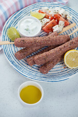 Blue and white plate with fresh uncooked lamb kofta kebabs, vertical shot on a white stone surface