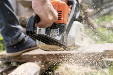 Male hands sawing old boards for firewood with a professional chainsaw, in a village yard. Winter preparation concept. Lifestyle.