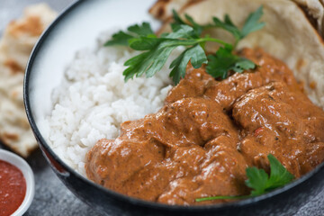 Closeup of a bowl with indian chicken makhani, white rice and flatbread, selective focus