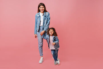 Good-humoured mom and daughter in denim jackets having fun together. Young mother and child holding...