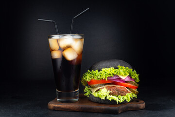 Big single cheeseburger with glass of cola on dark background